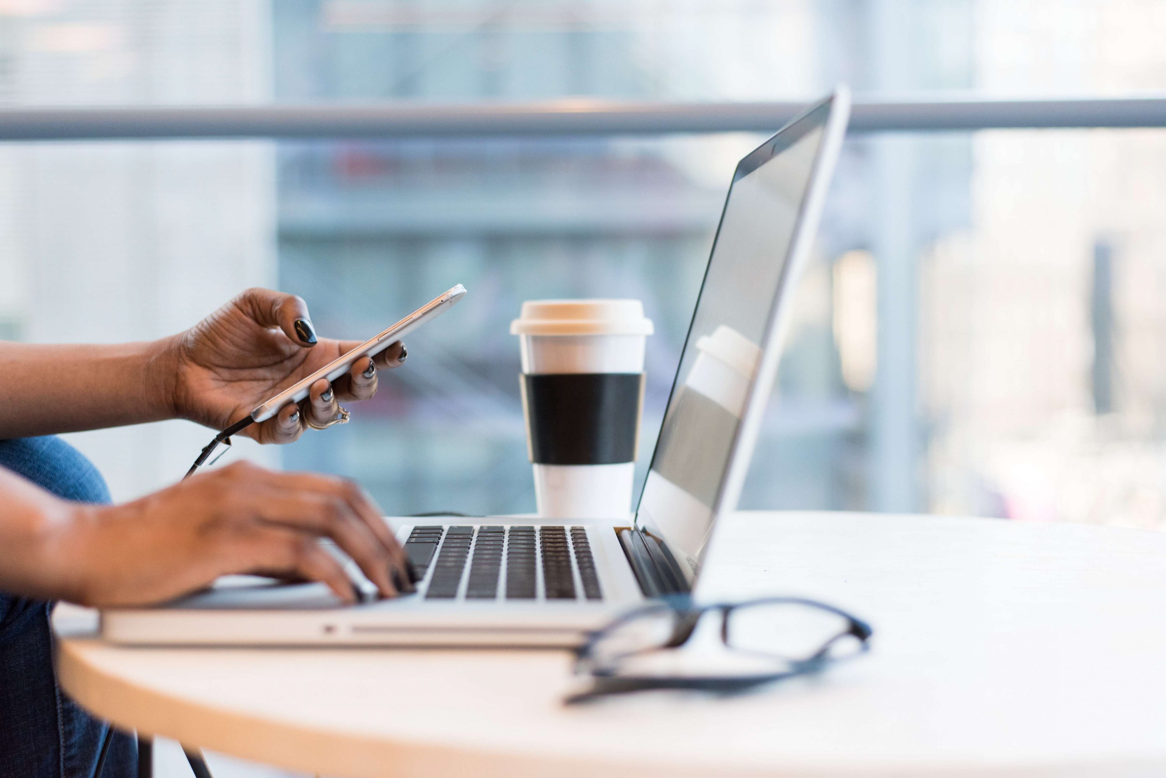 Woman's hand on notebook computer and holding phone.